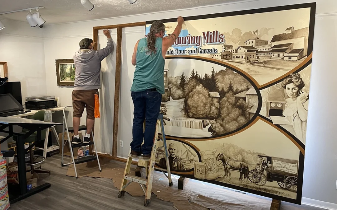 people unpacking a mural sized piece of art while on ladders